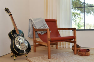 red leather and wood sling chair in living room with a throw blanket sitting next to a guitar