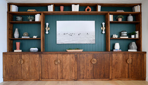 Wooden entertainment center with shelves and art mounted on a green wall.