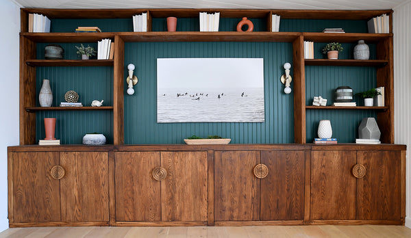 Wooden entertainment center with shelves and art mounted on a green wall.