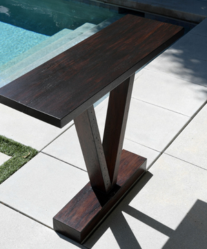 Wooden v-shaped side table photographed outside with pool and white tiles in the background