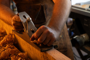 Person using a hand plane on wooden planks in a workshop setting